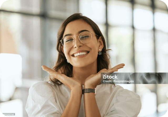 Smiling woman with glasses posing confidently indoors with hands under her chin, showing off her healthy smile