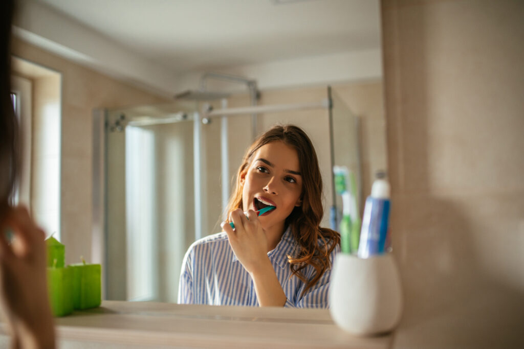 Woman brushing teeth in the mirror of her bathroom