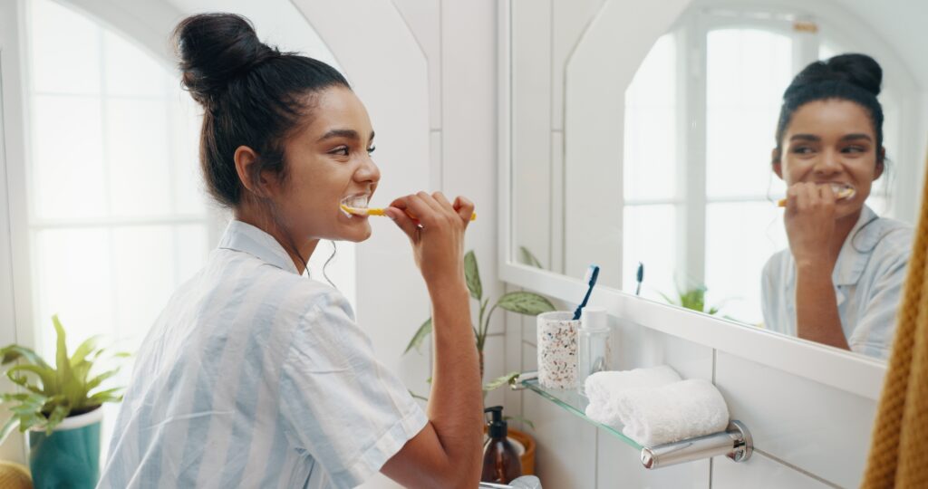 Woman brushing teeth using a mirror in the bathroom